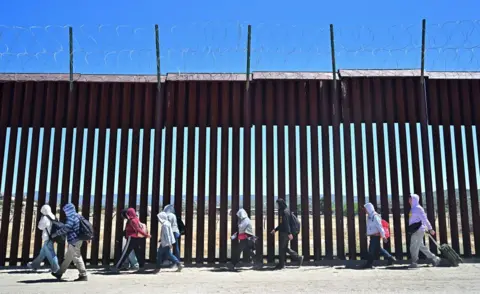 Mexican migrants walking on the US side of the border wall