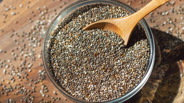 Chia seeds in a glass bowl with a spoon. Wooden board as a background. Healthy food concept, superfood, dietary supplements.