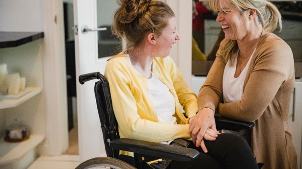 Mature mother is relaxing in the kitchen with her daughter who is in a wheelchair.